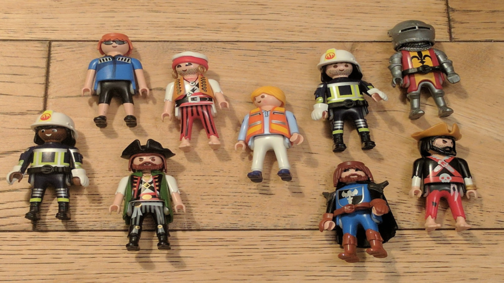 Photo of 9 Playmobil figures lying on a wooden floor. They're varied: firefighters, knights, pirates, cyclists.