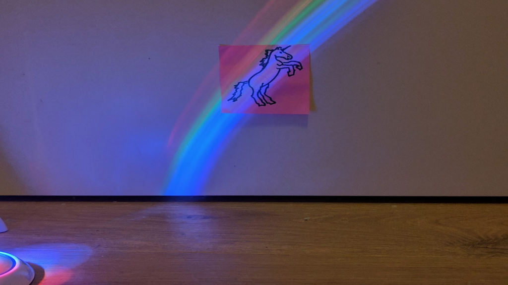 Same unicorn post-it as in previous photo, now lit by a lamp that's projecting a rainbow across it.