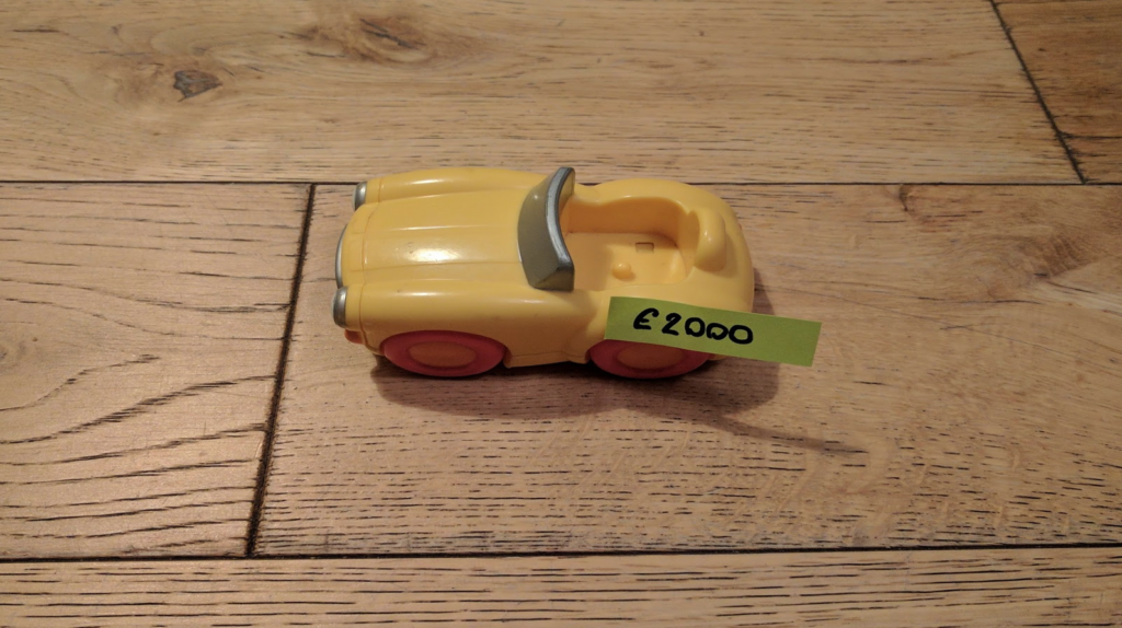 Photo of a simple toy car on a wooden floor. A small post-it saying "£2000" is stuck to the car.