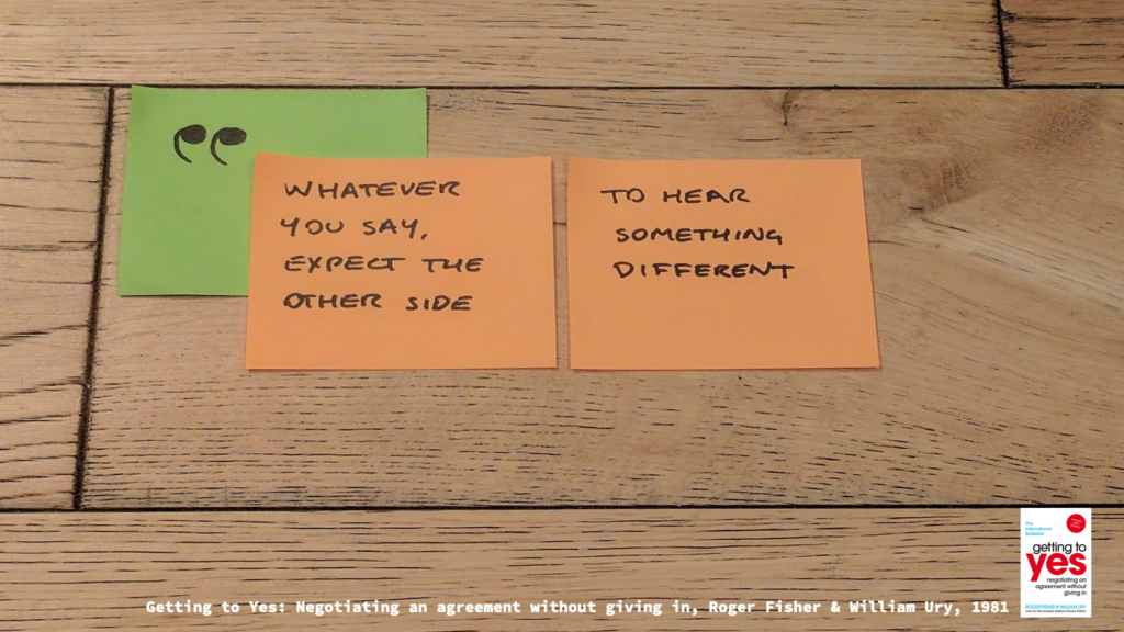 Post-its with a quote: 
"Whatever you say, expect the other side" 
"To hear something different"

Typed source at the bottom is "Getting to Yes: Nebotiating an agreement without giving in, Roger FIsher & William Ury, 1981"