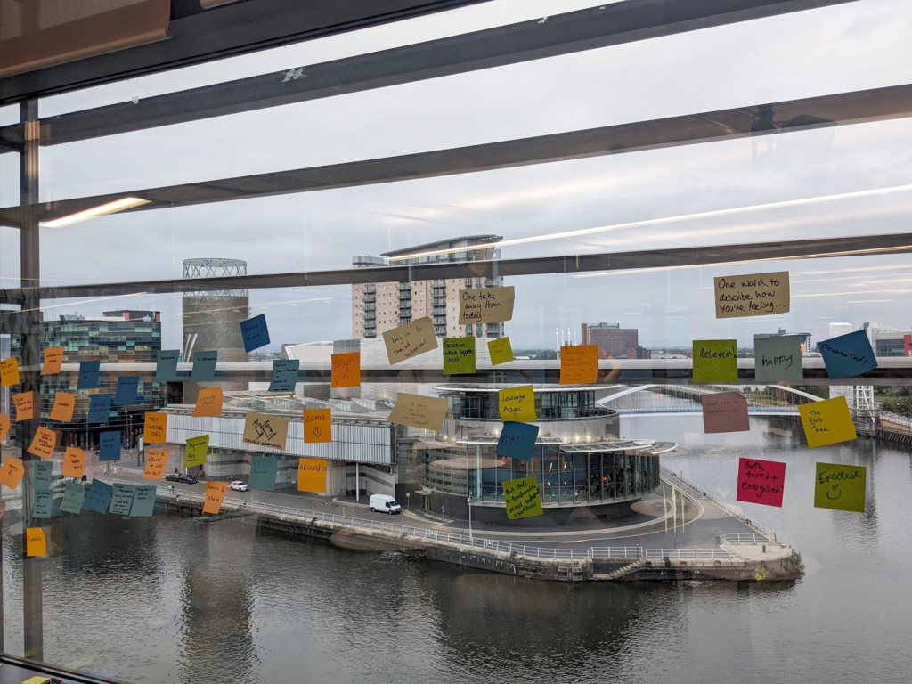 Window covered in post-its, too small to read. In the background: Water (Salford Quays), the Lowry theatre, other nice buildings and bridges.