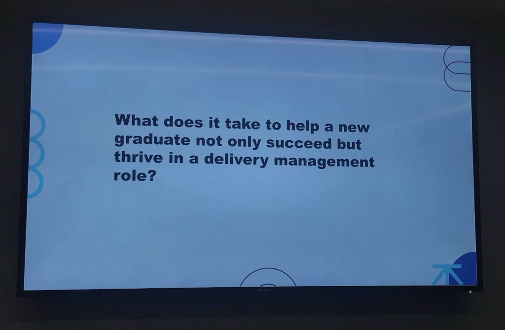 Photo of a slide, with text: "What does it take to help a new graduate not only succeed but thrive in a delivery management role?"

It's a white slide with various curved shapes round the outside.