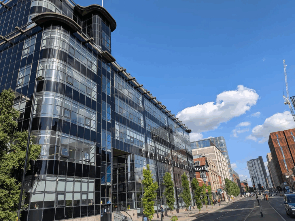 Photo of the outside of the Express building: it's a large glass building with rounded corners, strikingly different from the brick buildings elsewhere on the street. It's a surprisingly sunny blue sky.