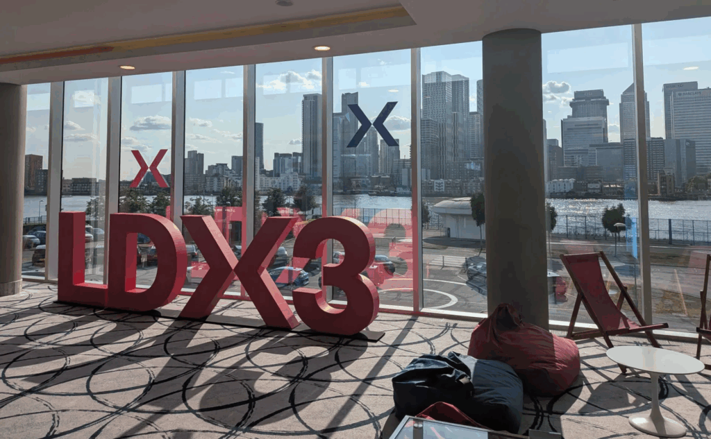 Photo of part of the conference venue: A wall of windows looks out across the sunny river Thames. Inside the room are deck chairs, beanbags, and a big free-standing conference logo.