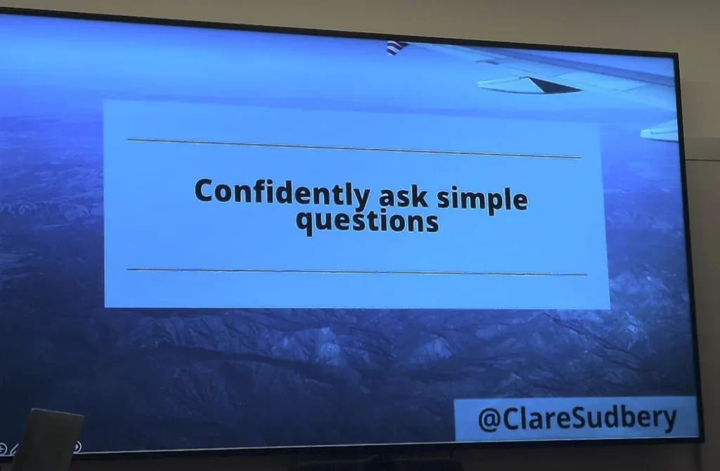 Slide saying "confidently ask simple questions". The slide background is a photo taken from high in the sky, with part of an aeroplane wing in the foreground and hills far below.
