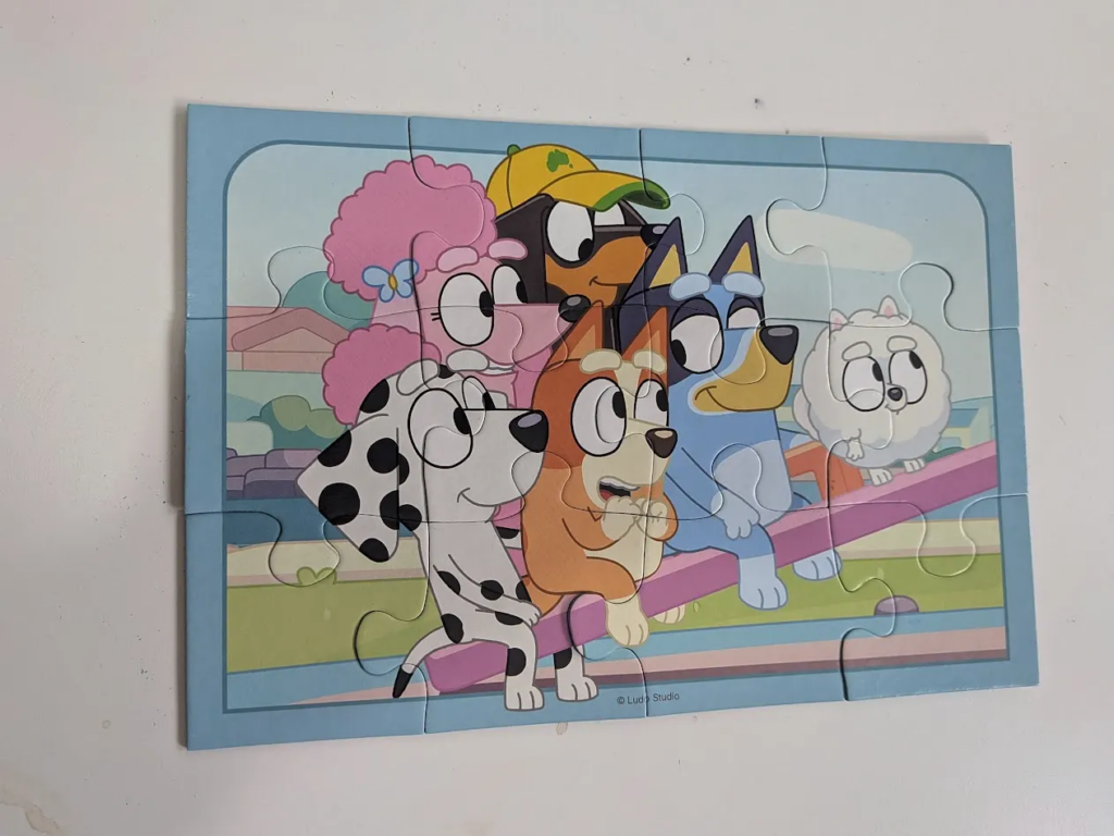 A completed jigsaw. It's a 12-piece puzzle, showing lots of characters from the Bluey cartoon on a seesaw.